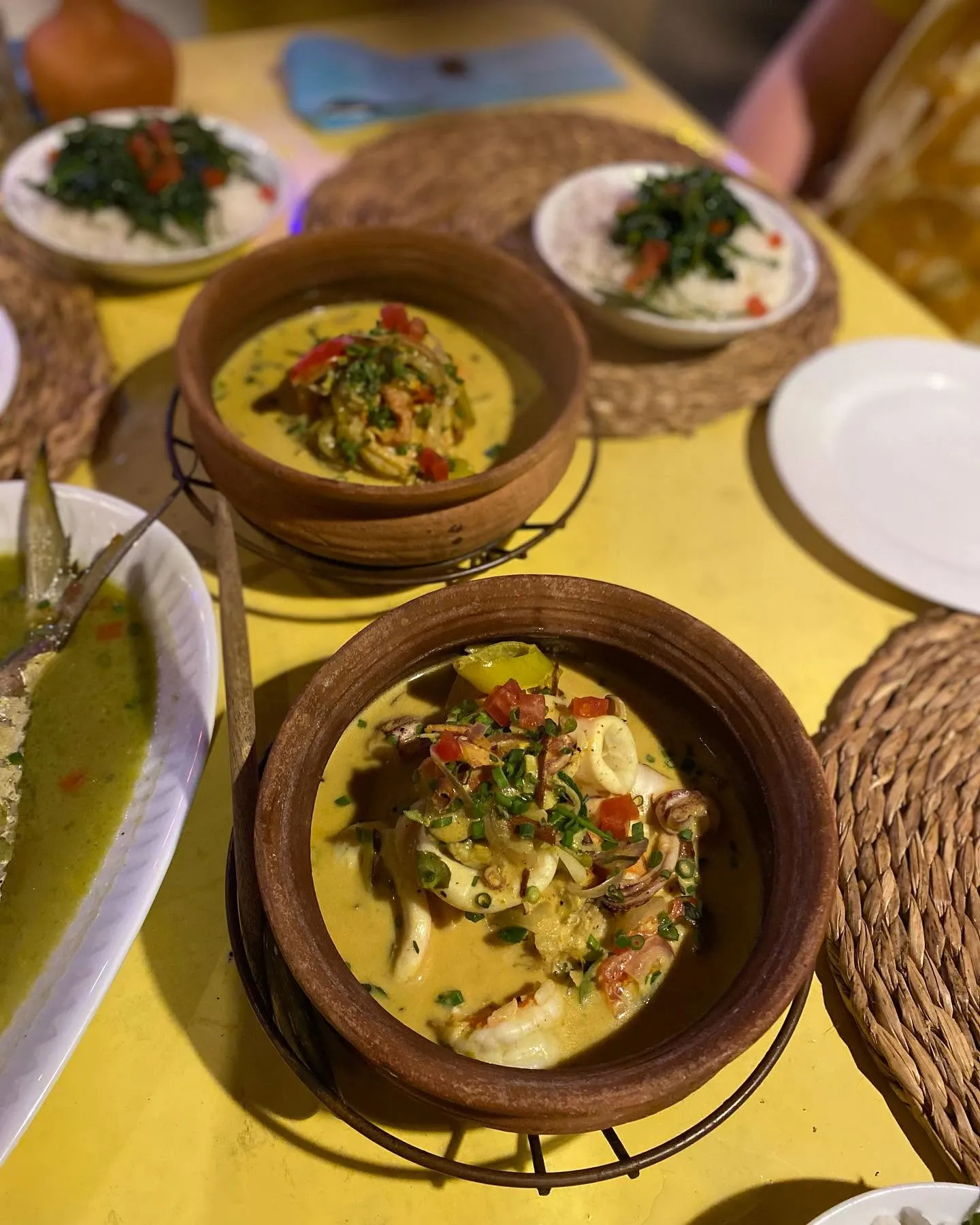 Clay pot seafood curry with squid, prawns and chili on a bright yellow tablecloth